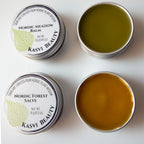 Kasvi Beauty Nordic Meadow Balm and Nordic Forest Salve. Two metal tins with lids open to expose the balm green color and golden color of the salve.