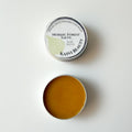 An open round metal tin of Kasvi Beauty Nordic Forest Salve, showing the golden-brown balm inside, with the lid placed above on a clean white background.