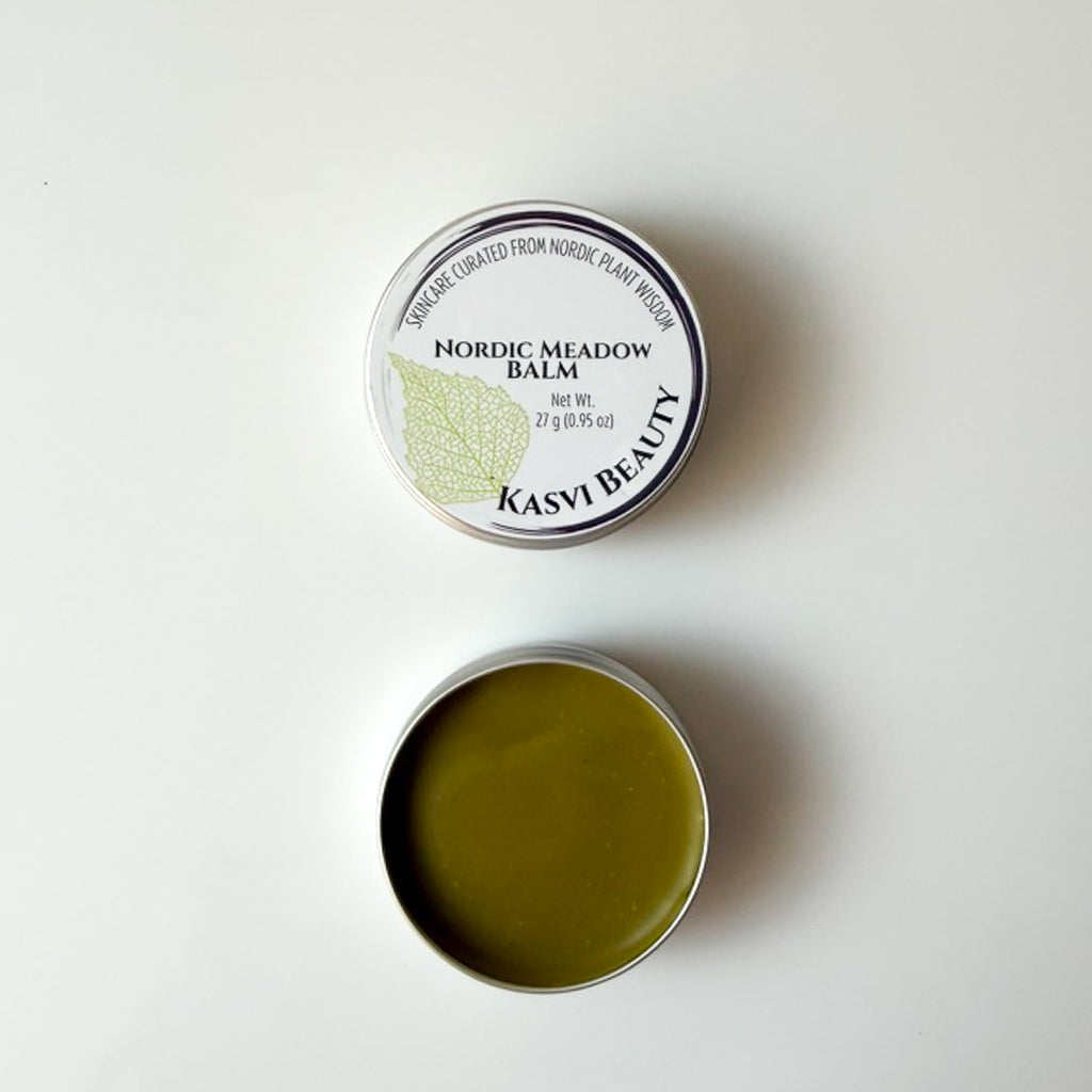 An open round metal tin of Kasvi Beauty Nordic Meadow Balm, showing the olive-green balm inside, positioned below its closed lid which features a white label with a green birch leaf graphic.