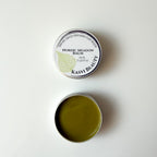 An open round metal tin of Kasvi Beauty Nordic Meadow Balm, showing the olive-green balm inside, positioned below its closed lid which features a white label with a green birch leaf graphic.